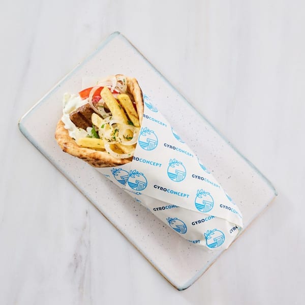 Gyro Concept's Greek gyro, wrapped in branded paper, filled with meat, fries, and vegetables.
