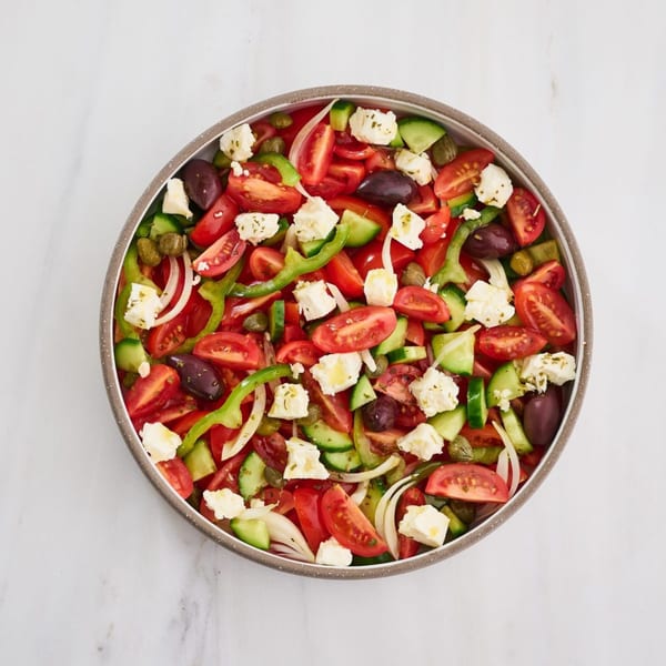 A vibrant Greek salad with tomatoes, cucumbers, bell peppers, feta, olives, and onions in a bowl.