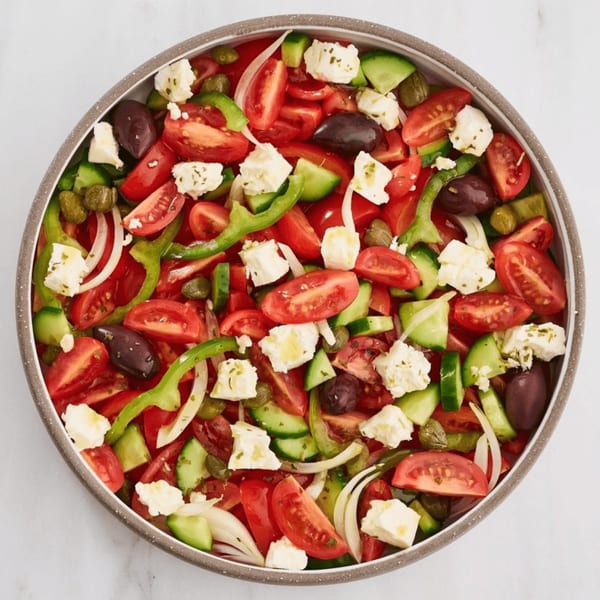 A vibrant Greek salad with tomatoes, cucumbers, feta, olives, onions, and capers in a bowl.