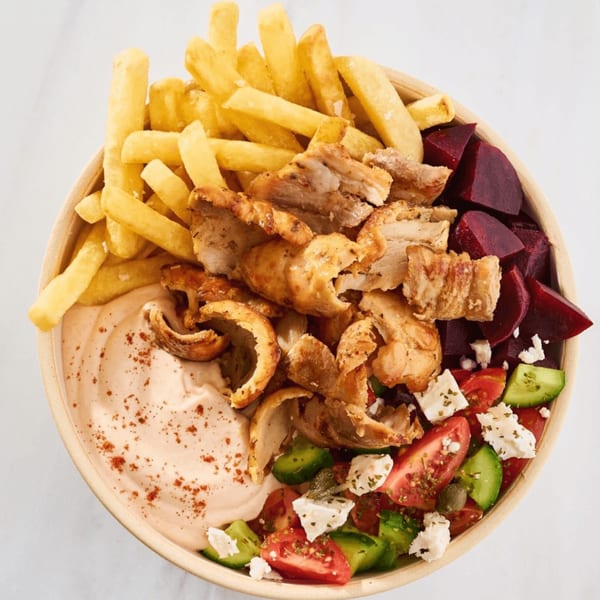 A Gyro Concept bowl with chicken, fries, beetroot, Greek salad, and a creamy sauce.