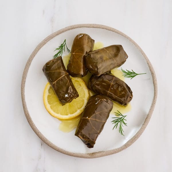 Five Greek dolmades, stuffed grape leaves, on a white plate with lemon slices and dill.