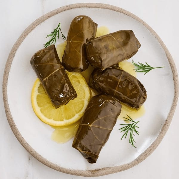 Five Greek dolmades, grape leaves stuffed with rice, garnished with lemon and dill on a white plate.