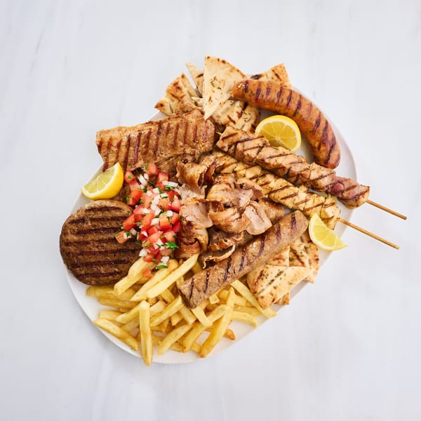A large Greek platter with grilled meats, pita bread, fries, lemon wedges, and tomato salsa.